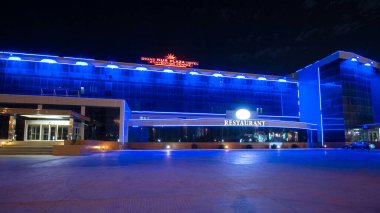 Aktau 'nun otel ve restoranlı gece hiperlapası. Aydınlatılmış Binalar Kazakistan 'ın Canlı Yüreğinde Akşam Gökyüzünü aydınlatıyor
