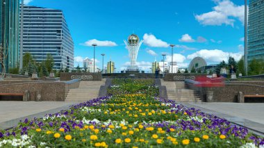 Nurzhol Bulvarı 'nda çiçekler. Arka planda Baiterek var. Kazakistan 'ın başkenti Nur-Sultan' da bir anıt, şehrin en önemli yerlerinden biri. Yazın mavi bulutlu gökyüzü