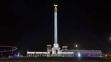 Stele anıtı Kazak Eli ve kuş Samruk geceleri ve Bağımsızlık Sarayı hiperhız ve trafik ön planda. Nur-Sultan şehri, Kazakistan