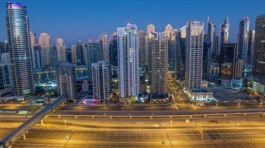 Dubai Marina gökdelenleri, güneş doğarken Dubai 'de JLT' den gündüz saatlerine kadar gökdelenler. Aydınlatılmış uzun gölgeli modern kuleler aşağı doğru ilerliyor ve Şeyh zayed yolunda trafik var..