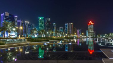 Geceleri Doha 'nın ufuk çizgisi. Yıldızlı gökyüzü Park Timelapse hiper hızından görünüyor, Katar. Aydınlatılmış gökdelenler ve kuleler çeşme suyuna yansıyor