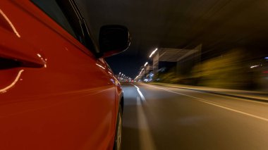 Hızlı arabanın yanından gelen bir drivelapse, gece caddesinde hızla ilerliyor. Işıklar yüksek hızda arabayı yansıtıyor. Modern bir şehrin hızlı ritmi. Bulanık hareket