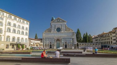 Santa Maria Novella Bazilikası 'nın Floransa' da eşkenar dörtgen zaman dilimi hiperhızlandırılmış görüntüsü. Çiçek yatakları ve yeşil çimenler. İnsanlar bankta oturuyor. Yazın mavi gökyüzü