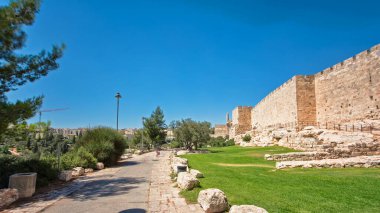 Antik kutsal Kudüs zaman tünelinin savunma duvarı. Parlak güneş tarafından aydınlatılan hiperhız. Yürüyüş yolu ve mavi gökyüzü yakınında harika yeşil çimenler.