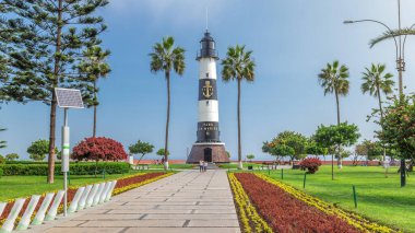Miraflores Aşkı Parkı 'ndaki deniz feneri anıtı zaman atlaması. Çiçekli ve palmiyeli yeşil çimenler. Güneşli bir günde sahil şeridi parkı. Lima, Peru