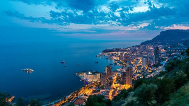 Monako 'nun havadan panoramik manzarası. Büyük Corniche yolundan geceye geçiş zamanı, Monako France. Akşam aydınlatması. Limanın suyundaki yansımalar