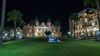 Monte Carlo 'da Grand Casino' yla birlikte Monaco 'da gece hiperhızlandırılmış zaman dilimi. Çevrede tarihi aydınlık binalar var. Tepedeki saat. Avuçlar yana..