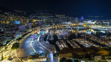 Monte Carlo 'nun Panorama' sı geceleyin Herkül Limanı ile Monako köyündeki gözlem güvertesinden hızla yükseliyor. Liman manzaralı, aydınlık binalar ve yatlar. Yolda trafik vardı.