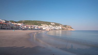 Sesimbra, Portekiz 'in küçük bir kasabasındaki iskeleden sahile, güneşli bir günde güneş batmadan önce mavi gökyüzü ile panorama zamanlaması hipervane