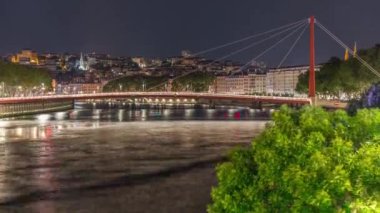 Saone Nehri üzerindeki kırmızı asma köprü ile Lyons şehir manzarasının gece zaman çizelgesi, aydınlatılmış kıyı şeridi gece boyunca suya yansıdı. Fransa