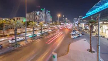 Riyad, Suudi Arabistan 'ın şehirsel gece zaman çizelgesinde aydınlık kuleler, gökdelenler, Kral Fahd Yolu ve yoğun trafik yer alıyor. Palmiyeler ve sokak lambaları alışveriş merkezinin yakınındaki ana otoyolda.
