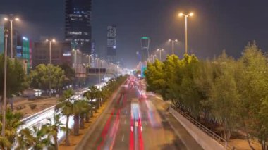 Suudi Arabistan, Riyad 'daki ikonik bükümlü gökdelenle King Fahd Yolu' ndaki yoğun karayolu trafiğinin hava takvimi görüntüsü. Aydınlanmış sokaklar ve ağaçlar. Dünyanın en uzun sekizinci büküm kulesi..