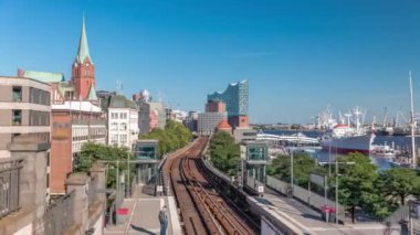 Almanya 'nın Hamburg kentindeki Landungsbrucken istasyonuna gelen trenler son sürat ilerliyor. Metroya binen insanlar mavi gökyüzünün altında Elbphilharmonie, liman ve marina ile panoramik manzara