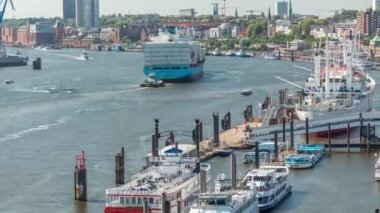 Almanya 'nın Hamburg kentinde Elbe nehir kenarının hava zaman çizelgesi. İskeleye yakın tekneler, Jan Fedder gezinti güvertesi, marina ve konteyner gemilerinin geçtiği manzara. Elbe Nehri kıyısındaki canlı şehir manzarası