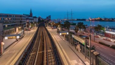 Almanya 'nın Hamburg kentindeki Landungsbrucken istasyonuna ulaşan trenlerin hava gününden geceye geçiş zamanı. Metroya binen insanlar, Elbphilharmonie, liman ve marina ile panoramik manzara