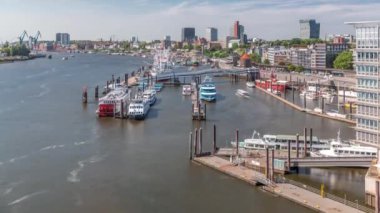 Almanya 'nın Hamburg kentinde Elbe nehir kenarının hava zaman çizelgesi. Rıhtımın yakınındaki Jan Fedder Gezinti Güvertesi, marina ve geçen gemilerle sahile manzara. Elbe Nehri kıyısındaki canlı şehir manzarası