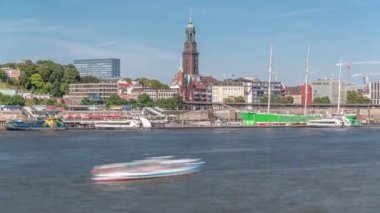 Elbe nehir kenarı ve Hamburg, Almanya 'daki St. Michaels kilise kulesinin panoramik zaman çizelgesi. İskeleye yakın teknelerle manzara, Jan Fedder gezinti güvertesi ve oradan geçen feribotlar. Nehir kenarındaki canlı şehir manzarası