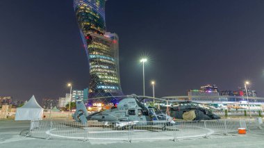 Abu Dabi, BAE - 25 Şubat 2023: IDEX Askeri Sergi Merkezi (ADNEC) IDEX Askeri Exibition 'ın günden geceye geçiş süresi, BAE. Helikopterlerin arkasında modern gökdelen var.