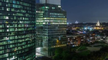 Brüksel 'deki cam cepheli ve parlayan pencereli modern gökdelenlerin ve kulelerin hava gece zaman çizelgesi. Arka planda Eglise Notre-Dame de Laeken 'in yer aldığı aydınlanmış şehir silueti. Belçika