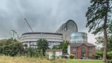 Brüksel 'deki Avrupa Mahallesi' ndeki binalar Avrupa Parlamentosu, Komisyon ve dramatik bulutlu gökyüzü altındaki kurumlarla aynı tarihe denk geliyor. Leopold Park ön planda kırmızı tuğlalı evle