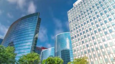 Modern ofis binalarının zaman çizelgesi. Parktaki yeşil ağaçlar tarafından çerçevelenmiş parlak mavi gökyüzü üzerinde yansımaları ve röfleleri olan cam gökdelenler. Brüksel, Belçika 'da güneş ışığı ve geçen bulutlar