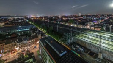 Brüksel Kuzey İstasyonu 'nun tren rayları, gelen ve giden trenlerle dolu. Schaerbeek şehir manzarası geceleri aydınlık binalar ve simgelerle doludur. Yükselen ay. Belçika