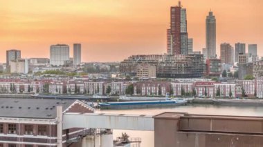 Günbatımında Rotterdam şehir merkezindeki modern binaların hava zaman çizelgesi, Hollanda. Finans bölgesinde kuleler ve gökdelenler, turuncu gökyüzü ile eski fabrika canlı bir ufuk çizgisi oluşturur