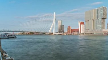 Hollanda, Rotterdam 'daki Maas Nehri' ni kapsayan Kuğu adlı Erasmus Köprüsü zaman dilimi. Hollands 'ın en büyük kablo destekli basküle köprüsü gökdelenleri, tekneleri ve bulutlu mavi bir arkaplanı var.