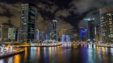 Dubai Marina gezinti güvertesinde yatlar ve modern kuleler ile deniz kenarındaki hiperhızlandırılmış sudan yansıtılır, Birleşik Arap Emirlikleri. Çevresinde yapay kanallar ve aydınlık gökdelenler olan bir bölge.