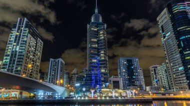 Dubai Marina kanalı üzerinde tekne ve köprüler bulunan, Dubai 'deki deniz kıyısından suya yansıyan palmiyeler ve modern kuleler, Birleşik Arap Emirlikleri' nin gece vakti aşırı hızlanması. Aydınlatılmış gökdelenler