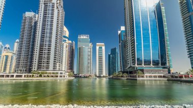 Rıhtımdaki palmiyeli gökdelenlerin hızlandırılmış görüntüsü. Jumeirah Gölü Kuleleri 'nde camla kaplı yerleşim yerleri Dubai, BAE' deki suya yansıdı. Rıhtımdan görüntüle