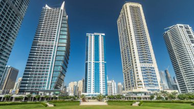 Rıhtımdaki palmiyeli gökdelenlerin hızlandırılmış görüntüsü. Dubai, BAE 'deki parkın yakınındaki Jumeirah Gölü Kuleleri' nde camla kaplı konut binaları. Parktan görüntüle