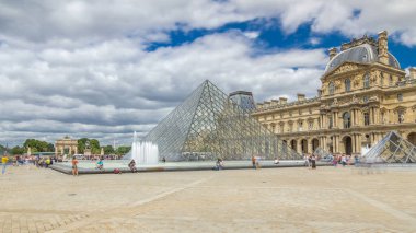 Camdan piramit ve Louvre Müzesi 'nin ana avlusu. Turistler yaz günü mavi bulutlu gökyüzüyle dolaşıyorlar. Paris, Fransa