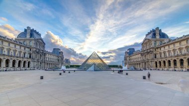 The Louvre museum pyramid during sunset timelapse in Paris, France. Colorful sky at summer day. People walk on square clipart