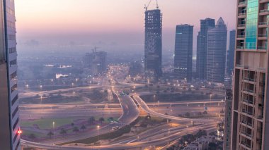 Havadan görünümü bir yol kavşak ve bir büyük şehir gece gün geçiş timelapse için modern kuleleri. Arabalar ve gökdelenler ile UAE Dubai Yat Limanı bölgesinin kentsel peyzaj.