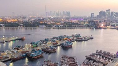 Dubai deresi manzarası günden geceye geçiş zamanı tekneler, yatlar ve yollarda trafik ve araba parkı olan modern binalar. Yukarıdan arka planda şehir merkezi olan hava üstü görüntüsü