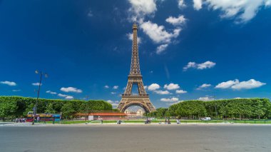 Paris 'teki Champs de Mars' taki Eyfel Kulesi. Zaman atlaması, Fransa. Yazın mavi bulutlu gökyüzü, yeşil çimenler ve etrafta trafik olan çeşme.