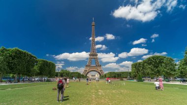 Paris 'teki Champs de Mars' taki Eyfel Kulesi. Zaman atlaması, Fransa. Yazın mavi bulutlu gökyüzü Yeşil çimlerle ve insanlar etrafta yürüyüp rahatlıyorlar
