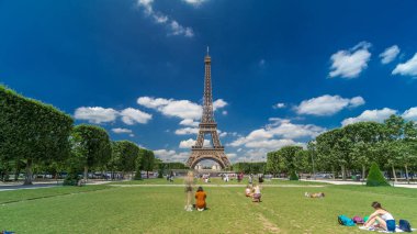 Paris 'teki Champs de Mars' taki Eyfel Kulesi. Zaman atlaması, Fransa. Yazın mavi bulutlu gökyüzü yeşil çimlerle kaplı ve insanlar etrafta dolaşıyor. İlerliyorum.