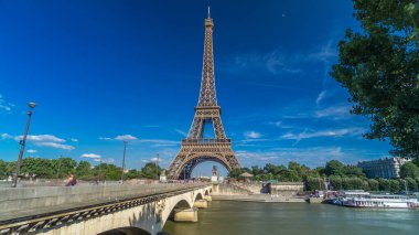Paris 'teki Siene Nehri üzerinde köprüsü olan Eyfel Kulesi. Zaman atlaması, Fransa. Yazın mavi bulutlu gökyüzü Yeşil ağaçlar ve köprüde yürüyen insanlar