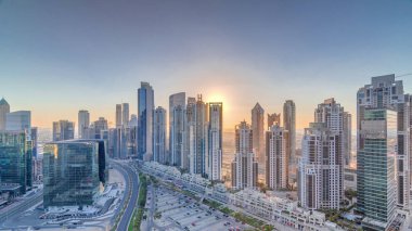 Günbatımında Business Bay, Dubai, Uae 'de bulunan birçok gökdelenle modern yerleşim ve ofis kompleksi. Körfez Bulvarı Parkı 'nın yanındaki büyük otoparkta arabalar ve trafik vardı.