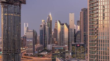 Dubai Finansal Merkezi 'nin aydınlatmalı modern gökdelenleri ile günden geceye geçiş zamanı. Şehir merkezinden hava görüntüsü, gün batımından sonra caddelerde trafik var.