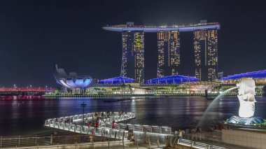 Merlion Çeşmesi, Singapur 'daki Marina Bay Sands Oteli' nin önüne su püskürtür. Köprüde insanlar var..