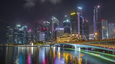 Esplanade Köprüsü ve şehir merkezindeki gökdelenler arka planda Singapur 'da gece vakti hızlandırılmış. Aydınlatılmış kuleler suya yansıyor