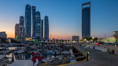 Al Bateen marina Abu Dhabi day to night timelapse after sunset with boats in harbor and illuminated modern skyscrapers on background clipart