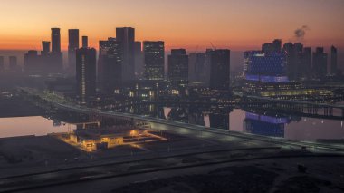 Abu Dabi şehrinin gökdelenleri aydınlanmadan önceki gökdelenleri gece gündüz geçiş zamanı. Çatıdan sisli bir sabahta köprüden hava manzarası ve yol trafiği