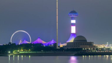 Abu Dabi 'de akşam, Marina Adası' ndan gece gündüz geçiş süresince Corniche 'in manzarası. Aydınlatılmış binalar ve su üzerindeki yansıma