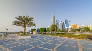 Abu Dabi 'nin sahil şeridi boyunca uzanan Corniche Bulvarı plajı parkında arka planda gökdelenler var. Avuçlar yana. Güneşli bir günde mavi gökyüzü