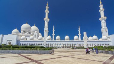 Birleşik Arap Emirlikleri 'nin başkenti Abu Dabi' deki Şeyh Zayed Büyük Camii zaman atlaması. Kubbeler ve minarelerle yan manzara. Ön planda çalılıklar. Güneşli bir günde mavi gökyüzü