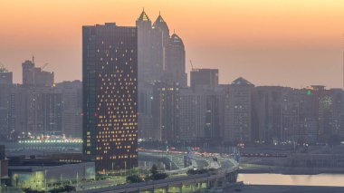 Skyscrapers on Al Reem and Al Maryah Island in Abu Dhabi day to night transition timelapse after sunset from above. Aerial cityscape from Al Reem Island with illuminated buildings clipart